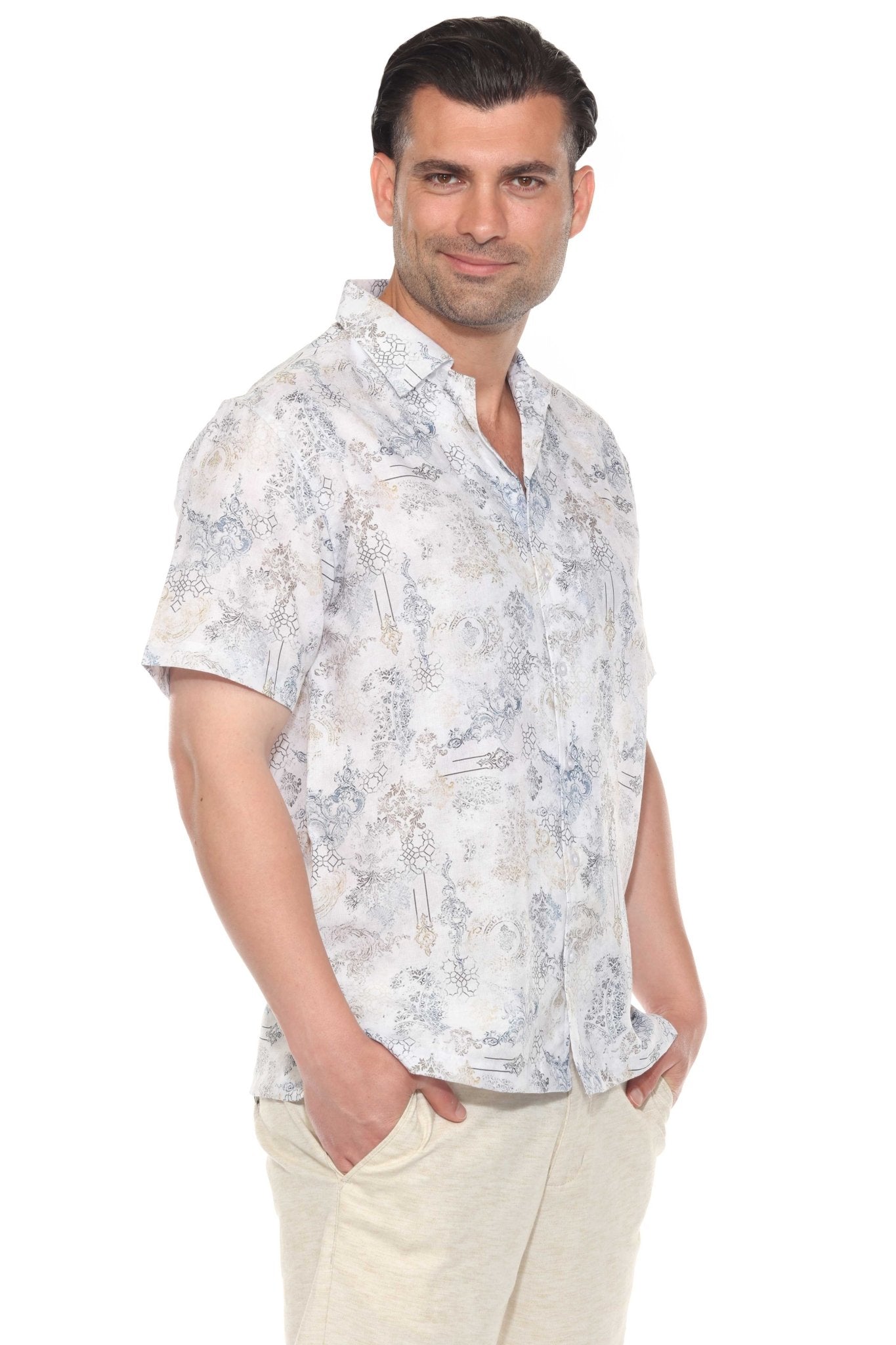 A man smiles in a white Men’s Tropical Print Resort Shirt with a light blue and tan pattern, standing with hands in pockets.