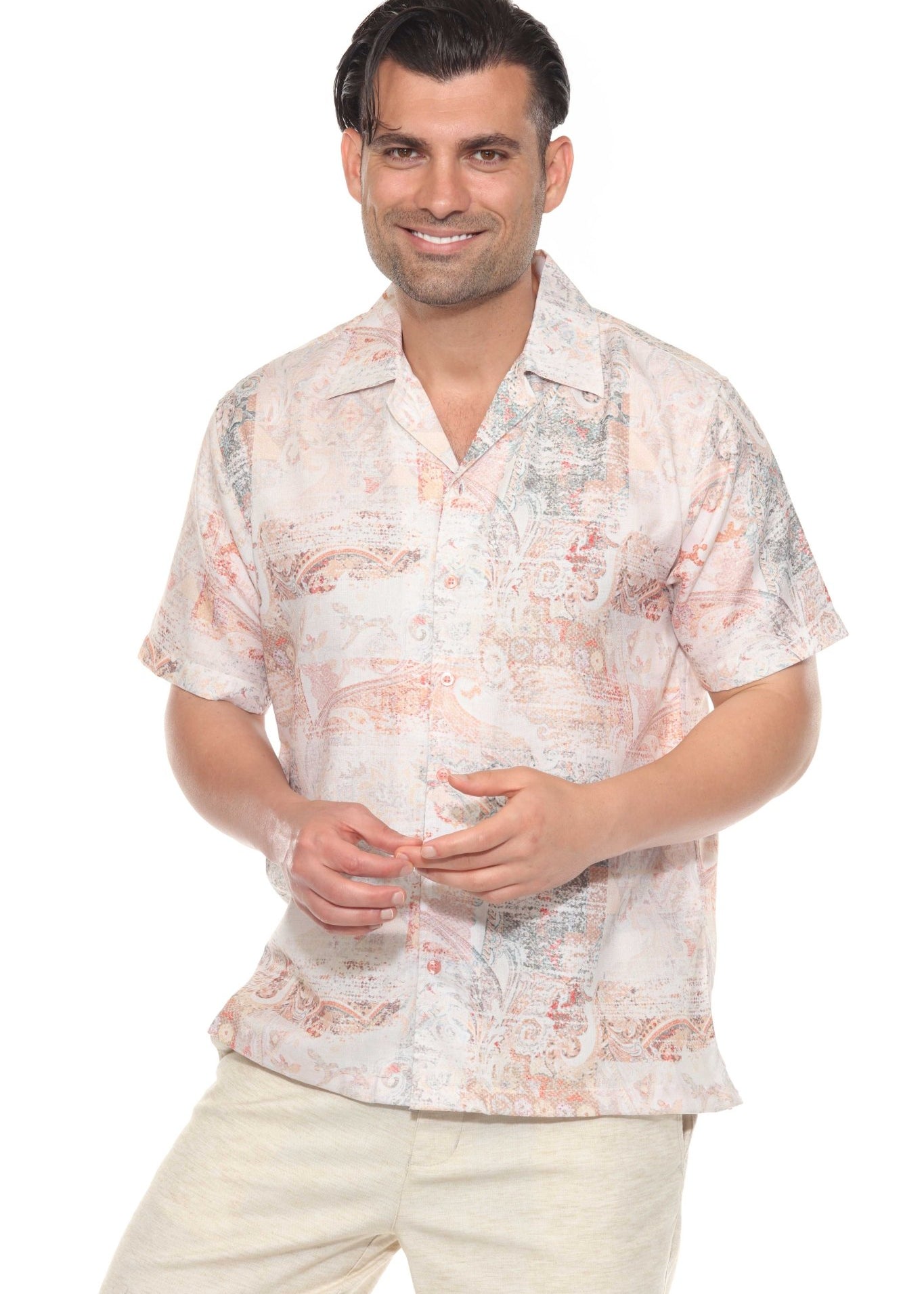 A smiling man wears a tropical print Men’s Resort Shirt, a short-sleeved, button-up top with a light pink and orange pattern on a white base.
