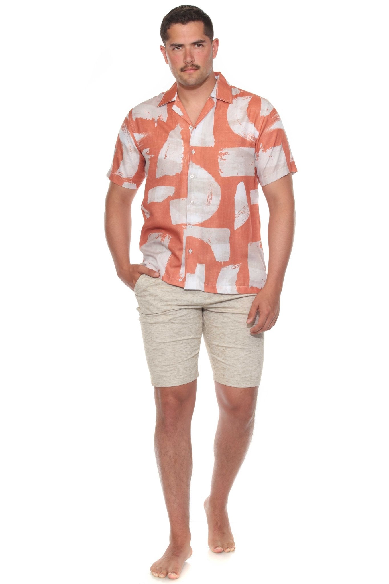A man wears a Men’s Tropical Print Resort Shirt, featuring an orange and white pattern, paired with light khaki shorts.