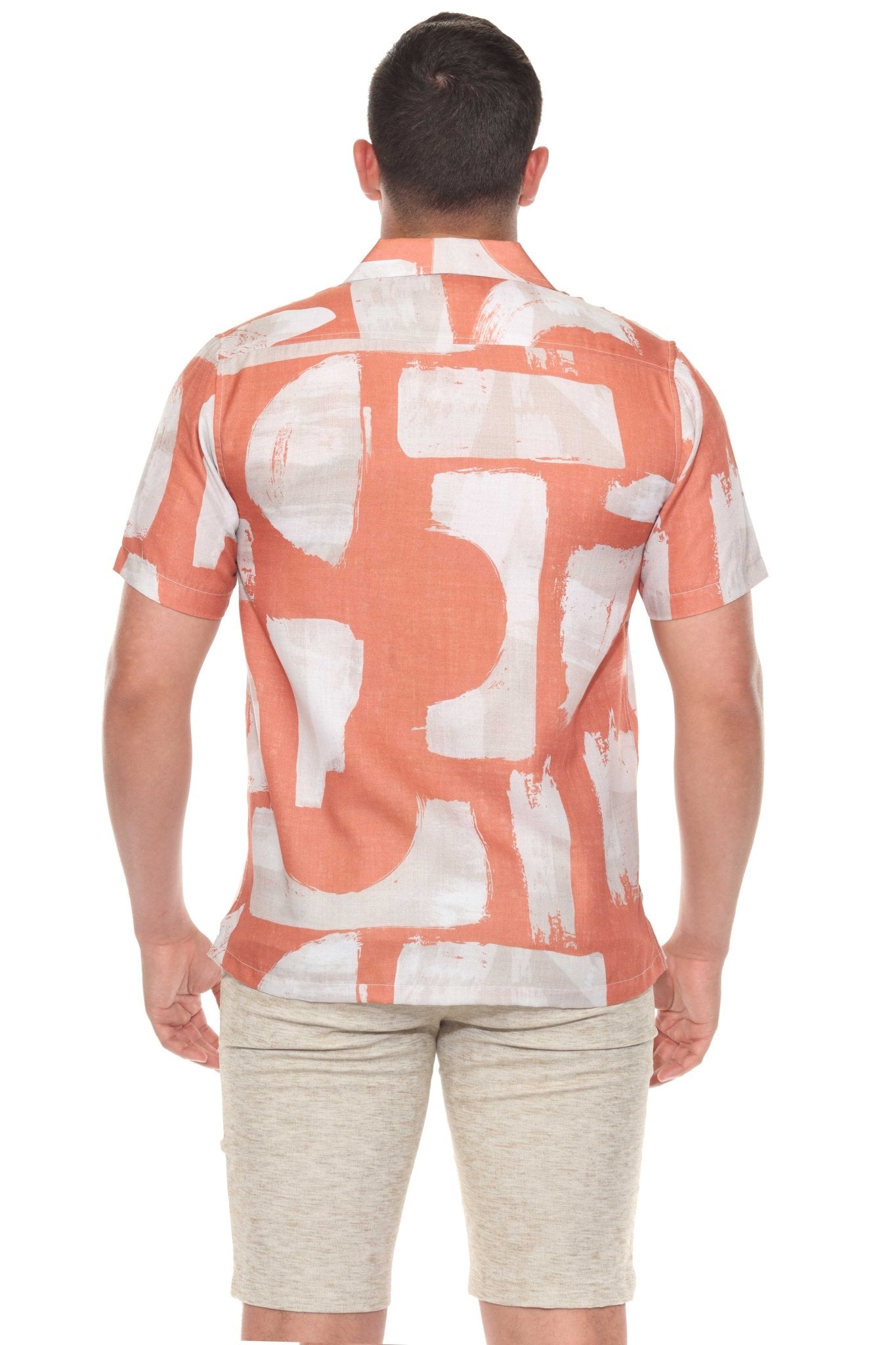 Back view of a man wearing the tropical print resort shirt, which is salmon colored with white geometric shapes.