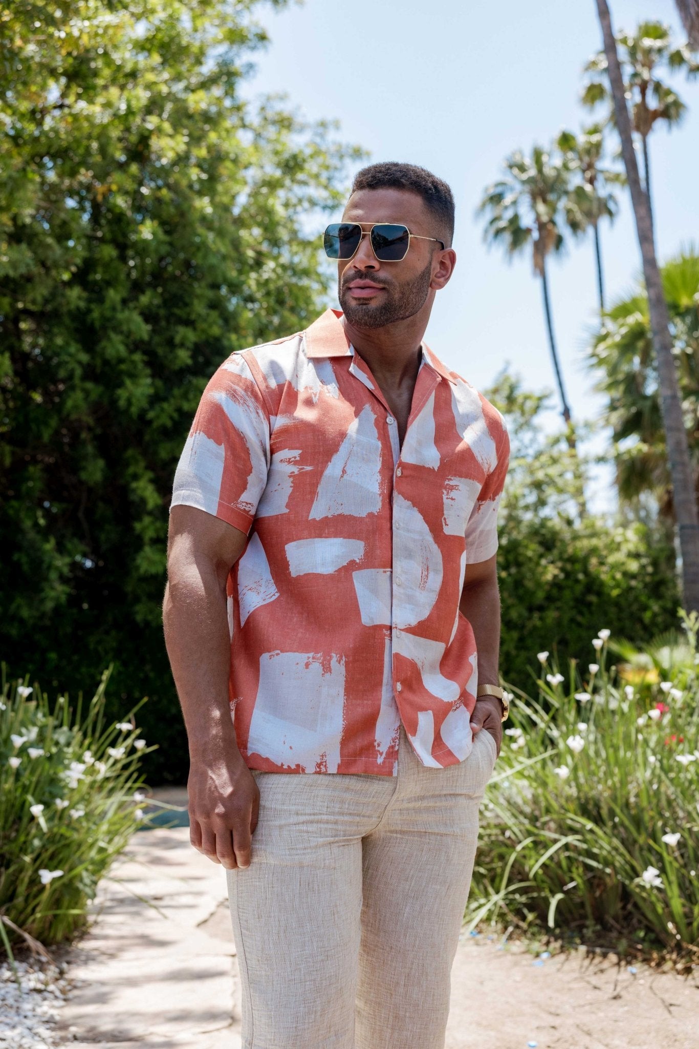Angled view of a man wearing an open coral tropical print Men's Resort Shirt with white splashes.