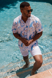 Man in a tie-dye shirt and white shorts standing by a pool