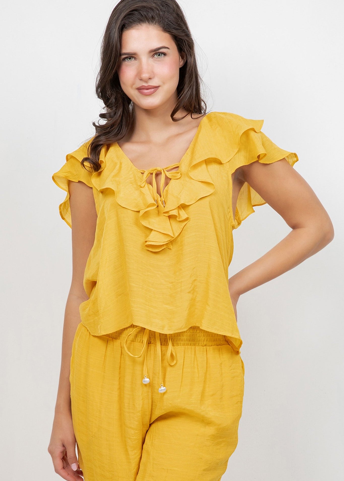 A woman wearing a yellow Ladies Casual Boho Ruffled Tie Blouse and matching pants smiles at the camera.