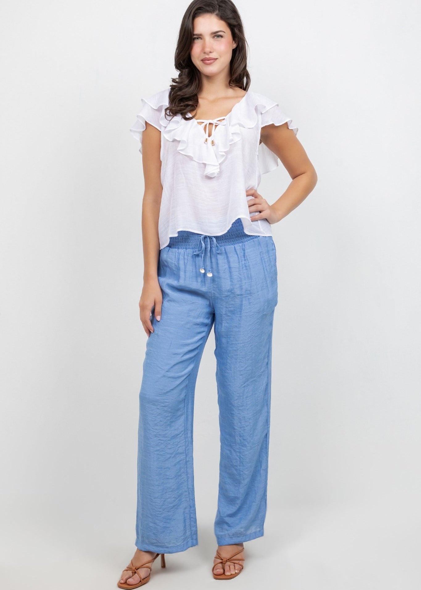 A model wears a white Ladies Casual Boho Ruffled Tie Blouse and blue pants, posing with hand on hip.