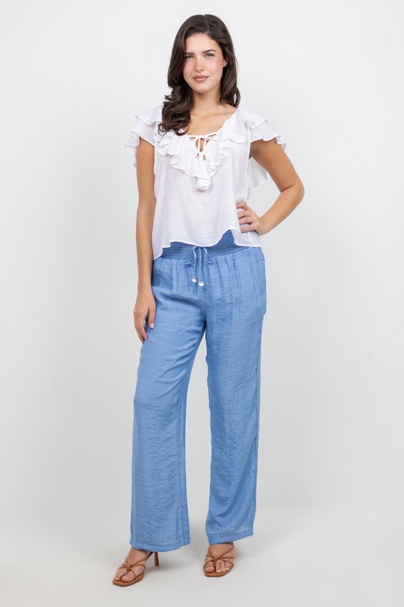 A model wears a white Ladies Casual Boho Ruffled Tie Blouse and blue pants, posing with hand on hip.