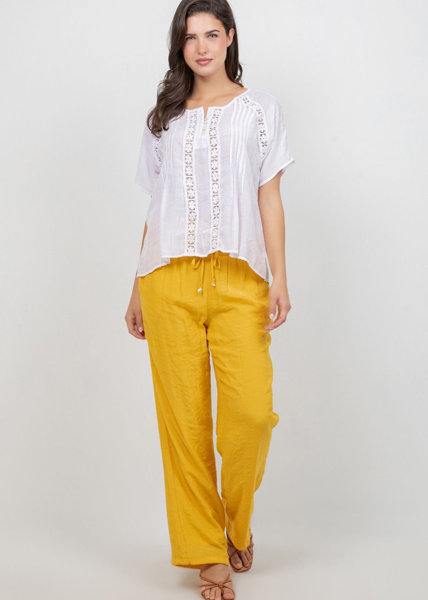 Front view of a woman wearing a white Ladies Boho Pleated Lace Panel Blouse and yellow pants.