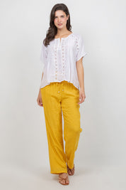 Front view of a woman wearing a white Ladies Boho Pleated Lace Panel Blouse and yellow pants.