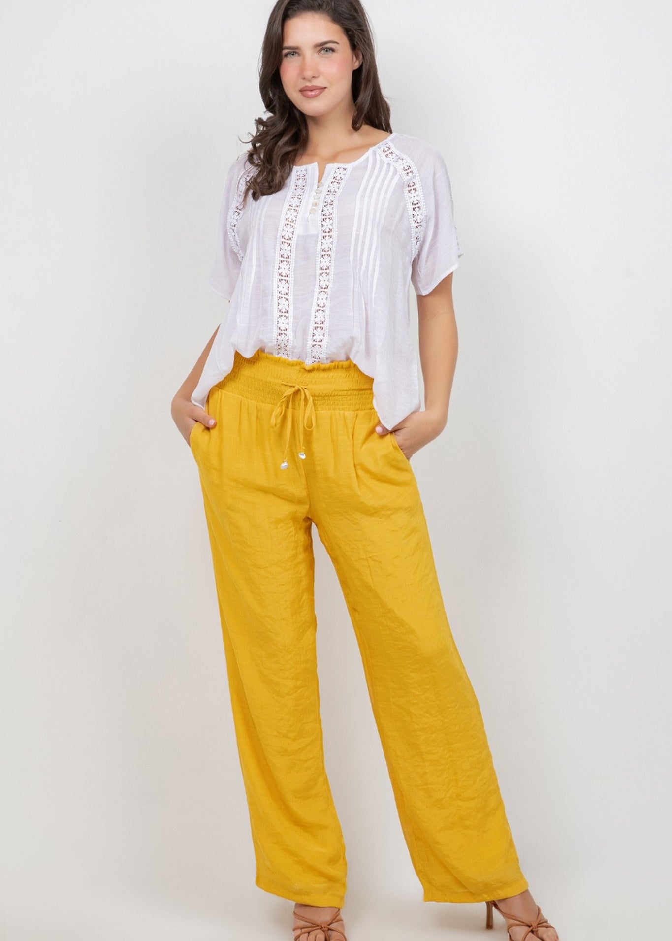 A model wears a white Ladies Boho Pleated Lace Panel Blouse tucked into bright yellow pants.