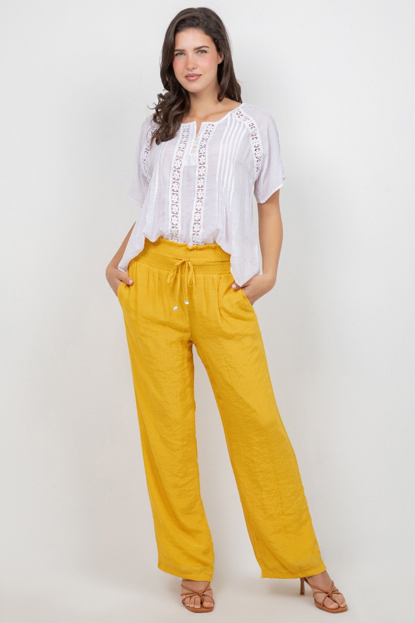 A model wears a white Ladies Boho Pleated Lace Panel Blouse tucked into bright yellow pants.