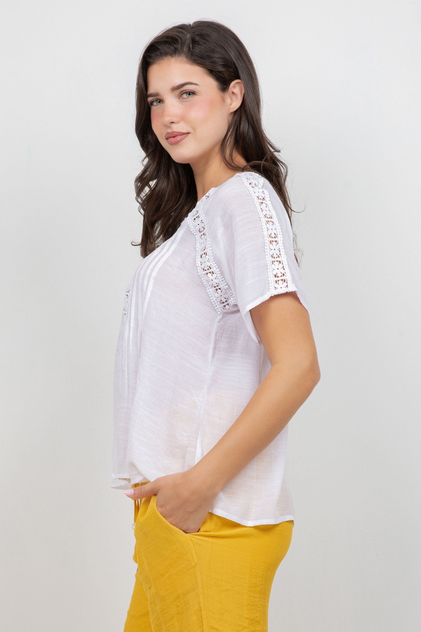 Profile of a woman wearing the white Ladies Boho Pleated Lace Panel Blouse with lace detail on sleeves and shoulders.
