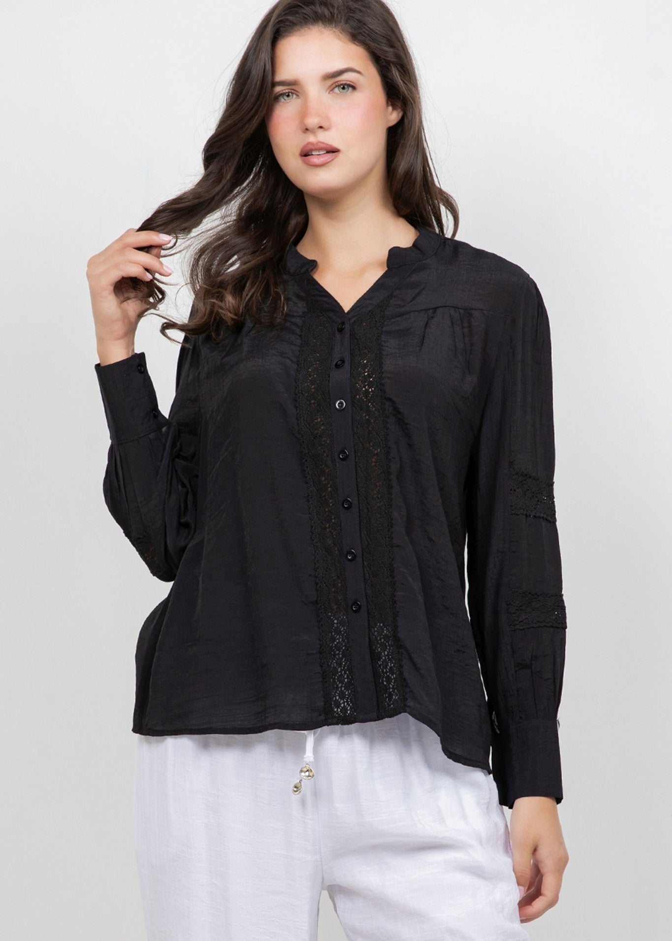 A woman models the Ladies Boho Lace Panel Pleated Long Sleeve Blouse in black with lace detail down the front.
