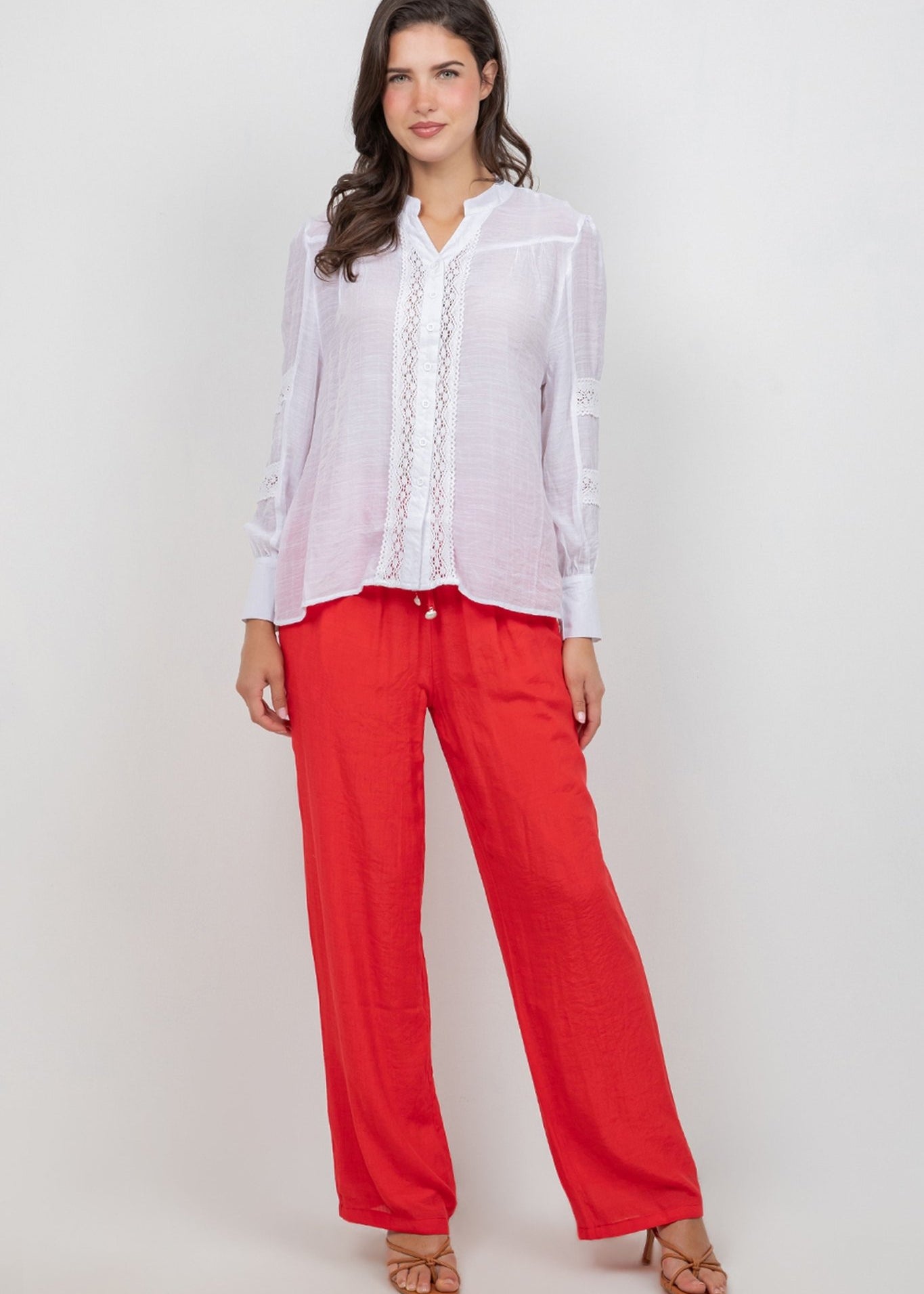 A woman models a white Ladies Boho Lace Panel Pleated Long Sleeve Blouse with bright red pants.
