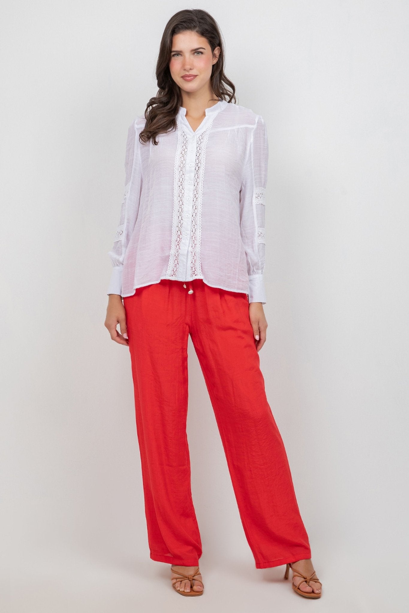 A woman models a white Ladies Boho Lace Panel Pleated Long Sleeve Blouse with bright red pants.