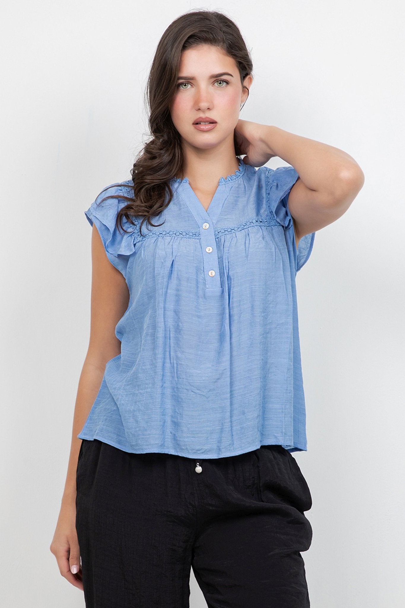 Model wearing a light blue Ladies Boho Flutter Sleeve Button Blouse and black pants.