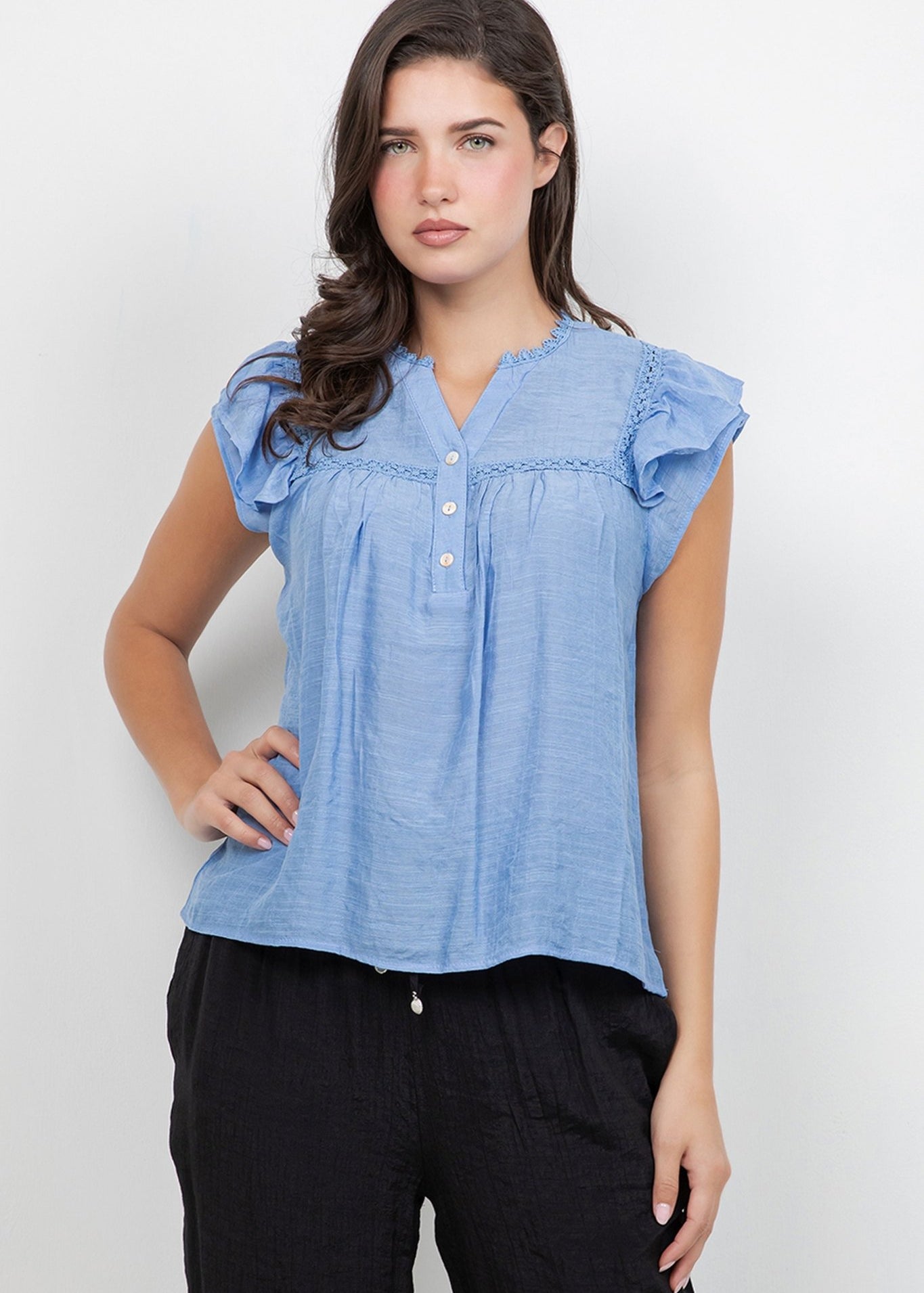 Front view of a woman wearing a light blue Ladies Boho Flutter Sleeve Button Blouse with crochet trim and black pants.