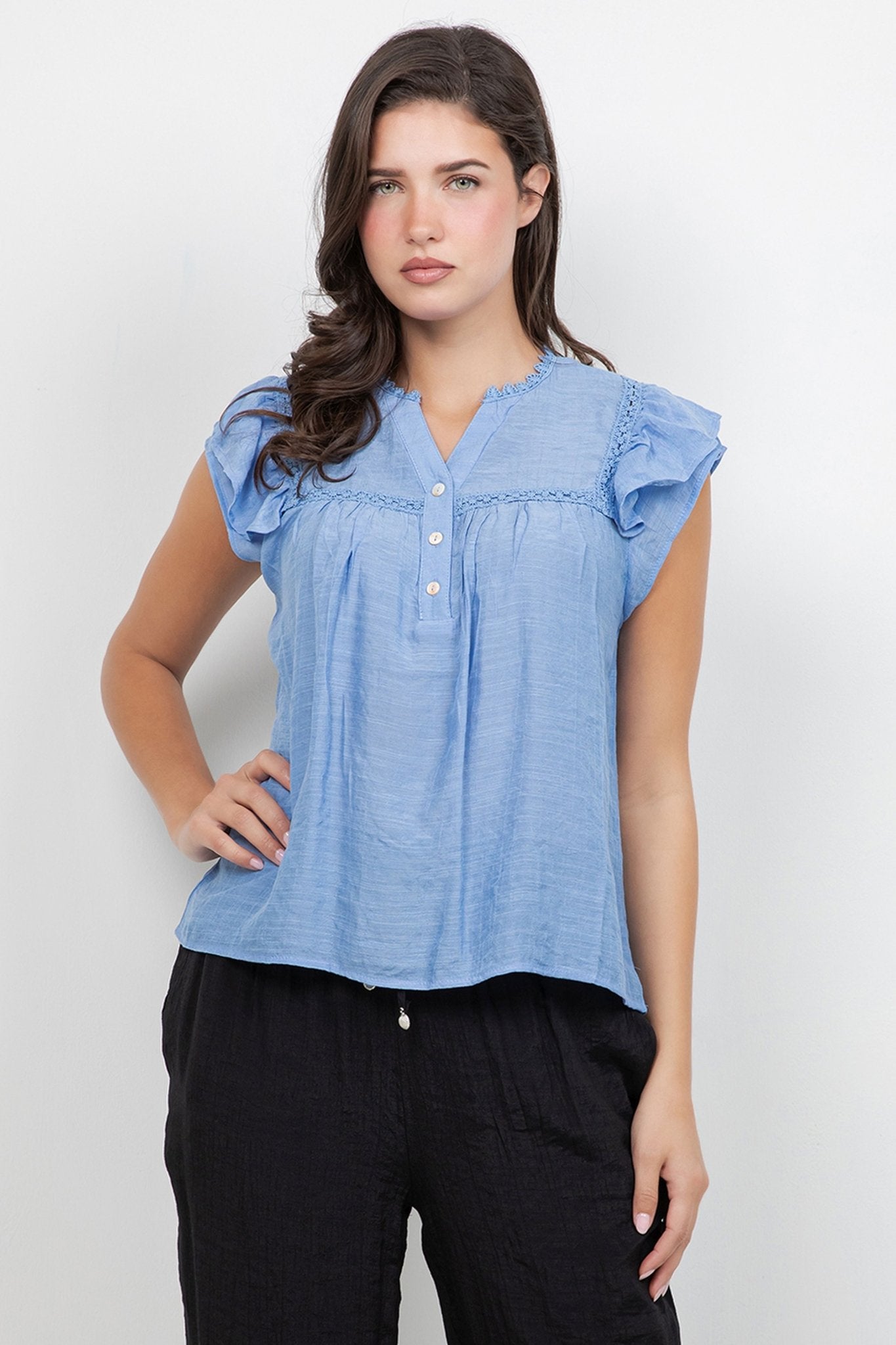 Front view of a woman wearing a light blue Ladies Boho Flutter Sleeve Button Blouse with crochet trim and black pants.