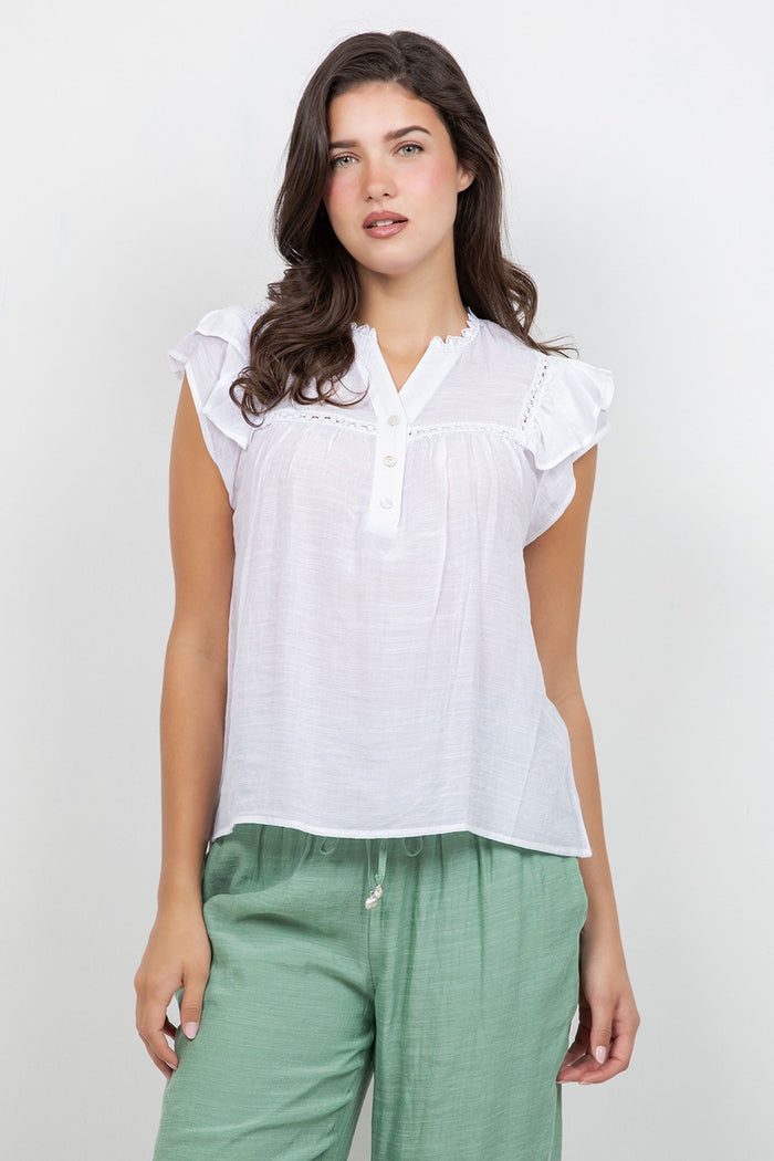 A woman wears a white Ladies Boho Flutter Sleeve Button Blouse and green pants, front view.