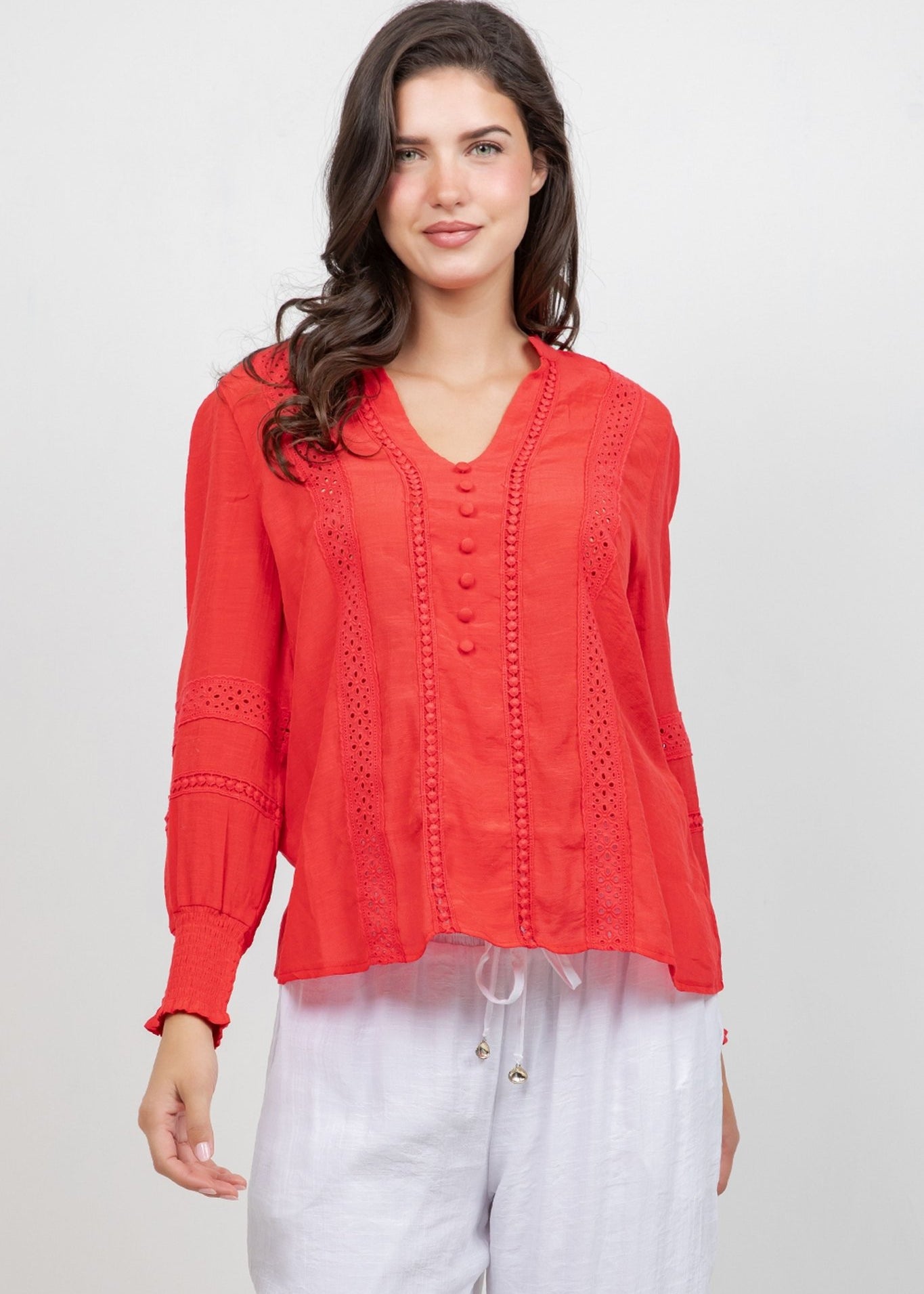 Front view of a woman wearing a red Ladies Boho Lace Panel Long Sleeve Blouse with eyelet details and white drawstring pants.