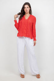 A woman poses wearing a red Ladies Boho Lace Panel Long Sleeve Blouse with white pants.