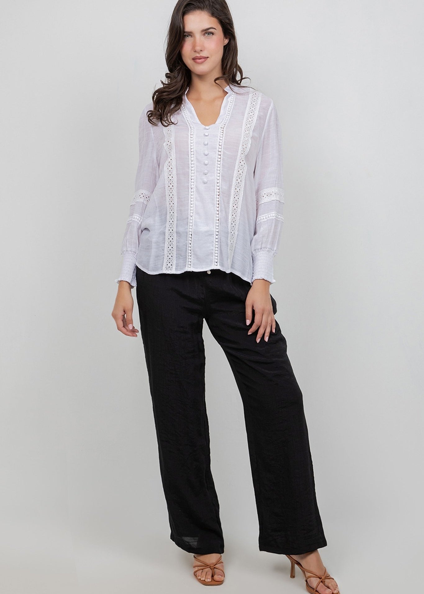 A woman models a white Ladies Boho Lace Panel Long Sleeve Blouse with lace detailing and black trousers.