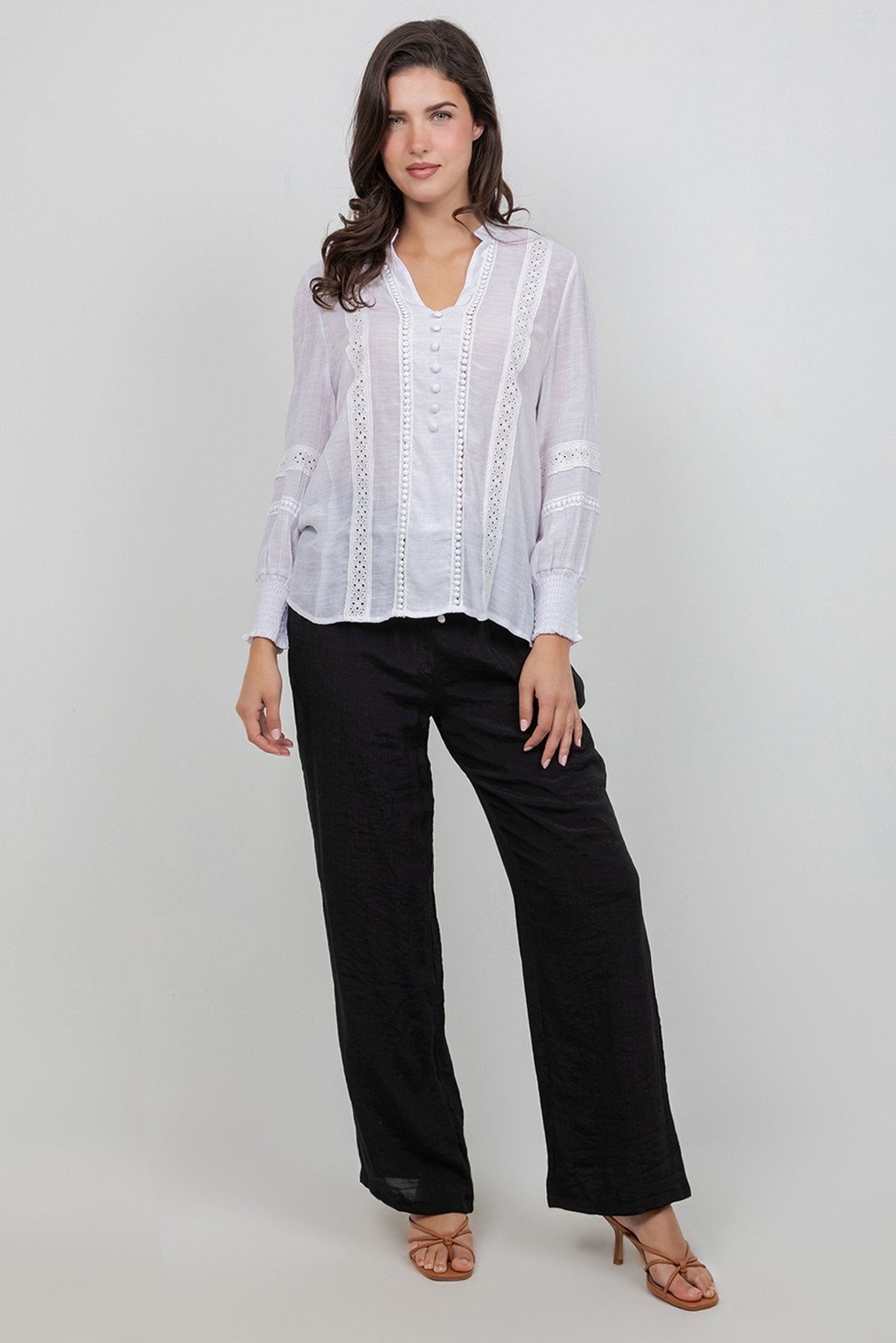 A woman models a white Ladies Boho Lace Panel Long Sleeve Blouse with lace detailing and black trousers.