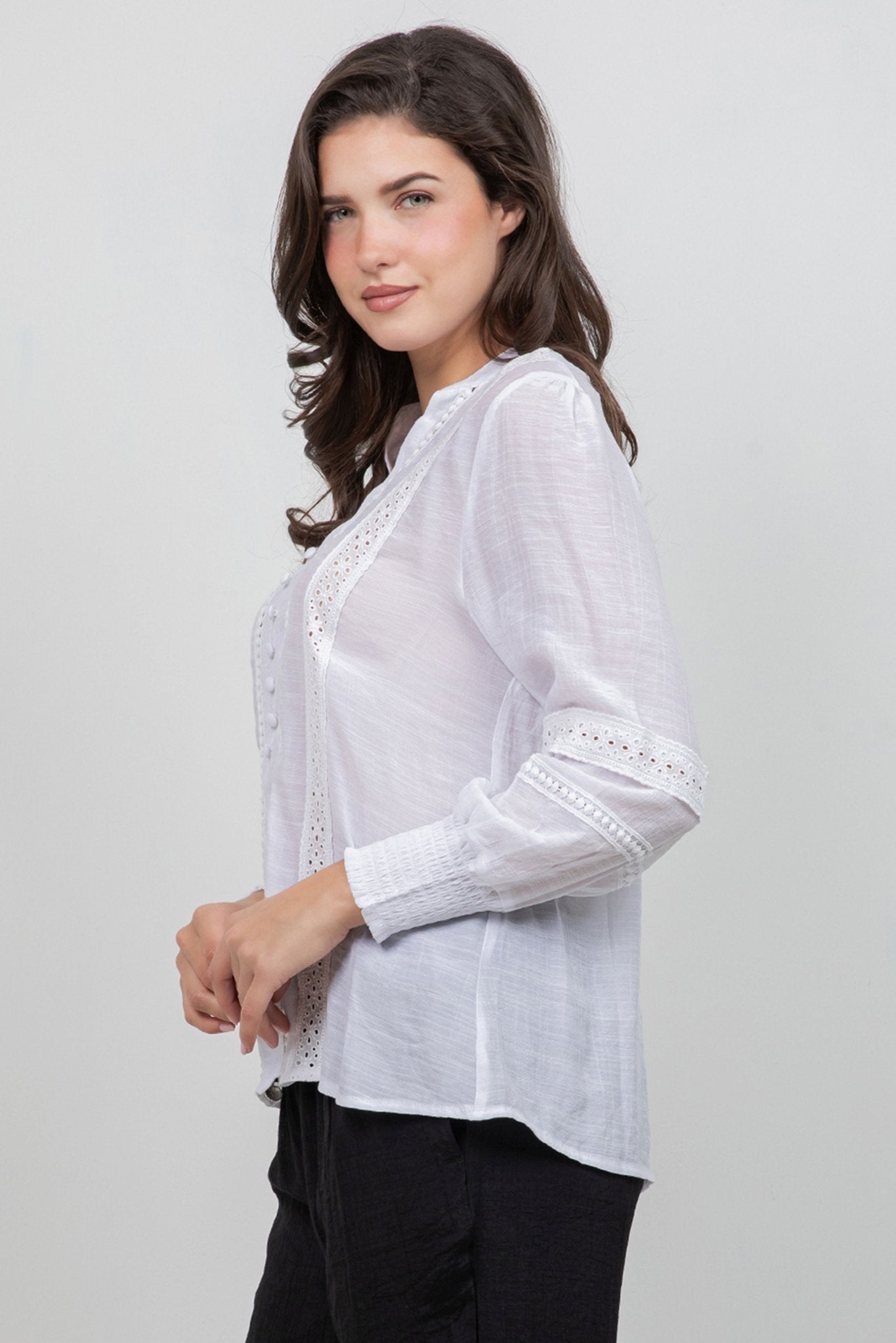 A woman wears a white Ladies Boho Lace Panel Long Sleeve Blouse with lace details and buttons, paired with black pants.