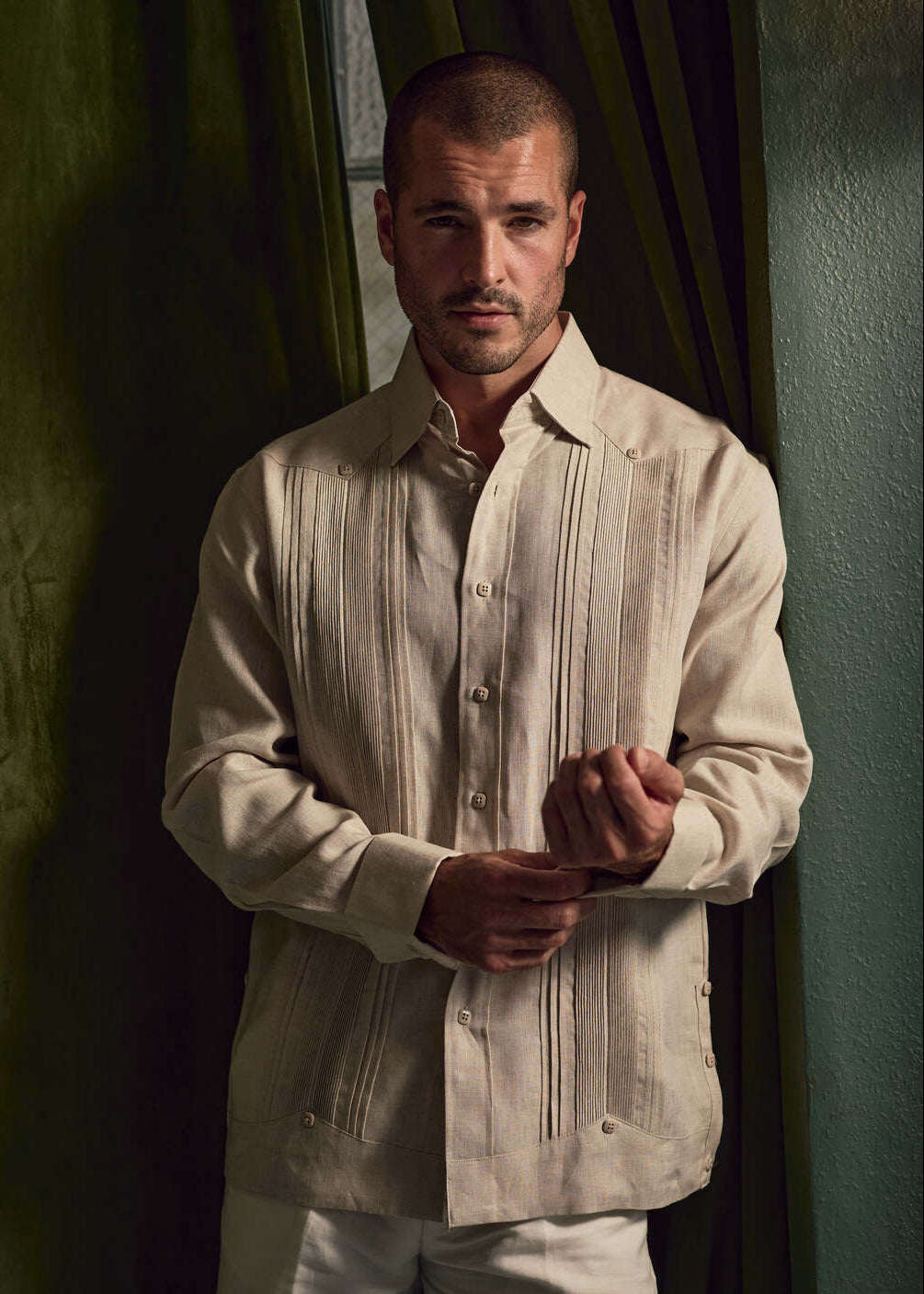 A man adjusting the cuff of a beige Men's Linen Formal Guayabera Long Sleeve Pleated Shirt.