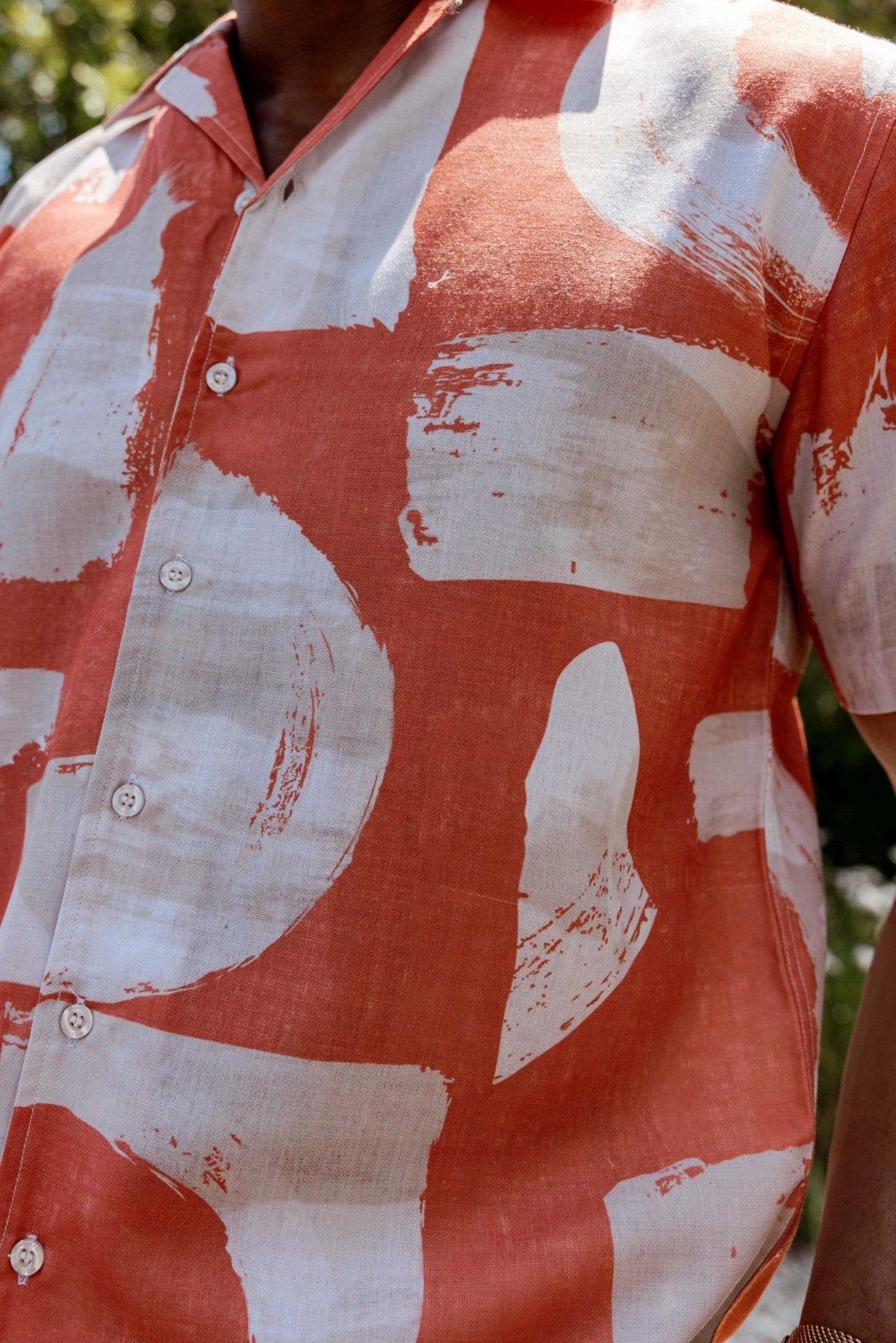 Close-up of a Men’s Tropical Print Resort Shirt in coral and white with a bold, abstract pattern, visible buttons, and short sleeves.