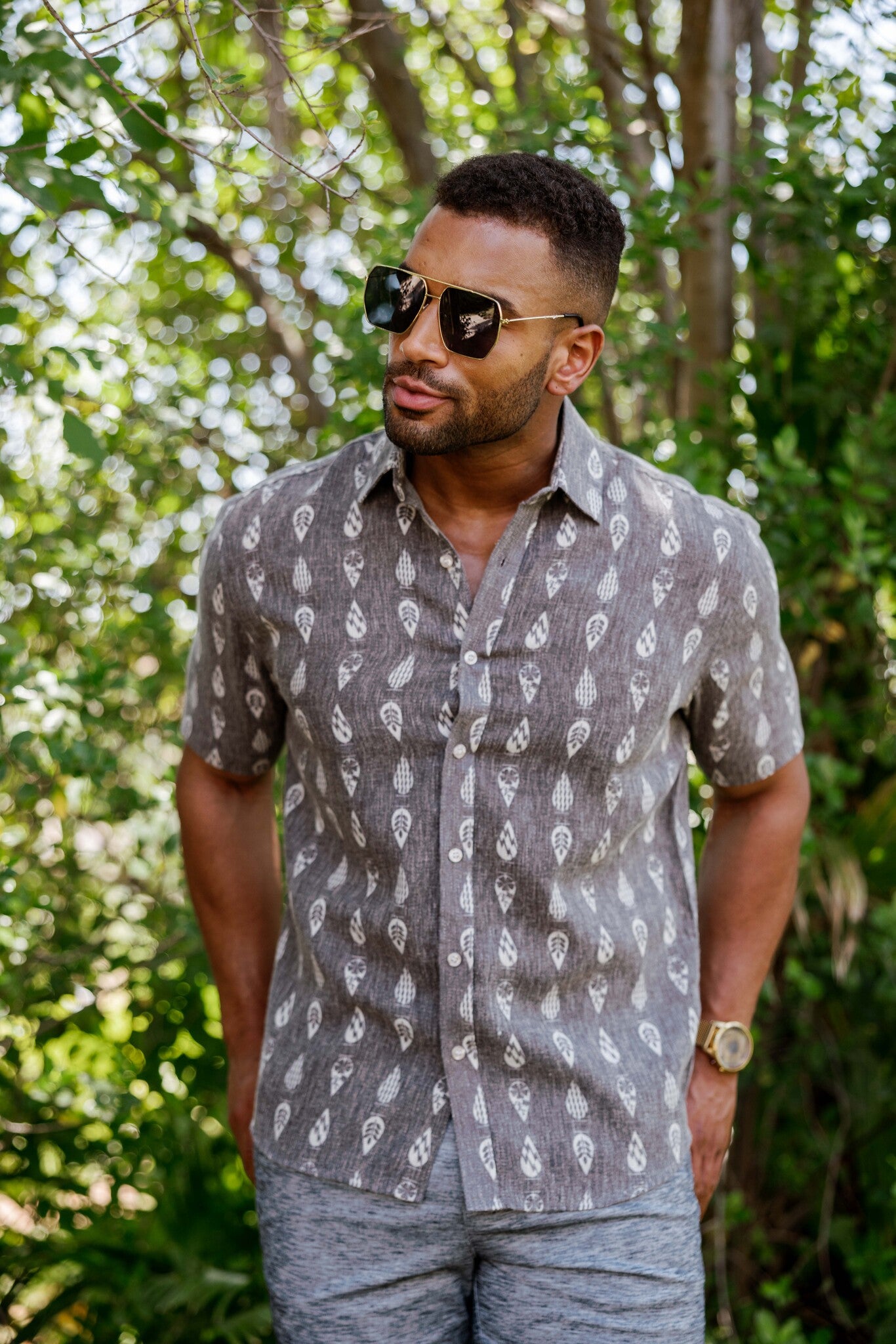 A man wears a Menâ€™s 100% Cotton Resort Print Short Sleeve Button-Up Shirt with a grey leaf-like print.