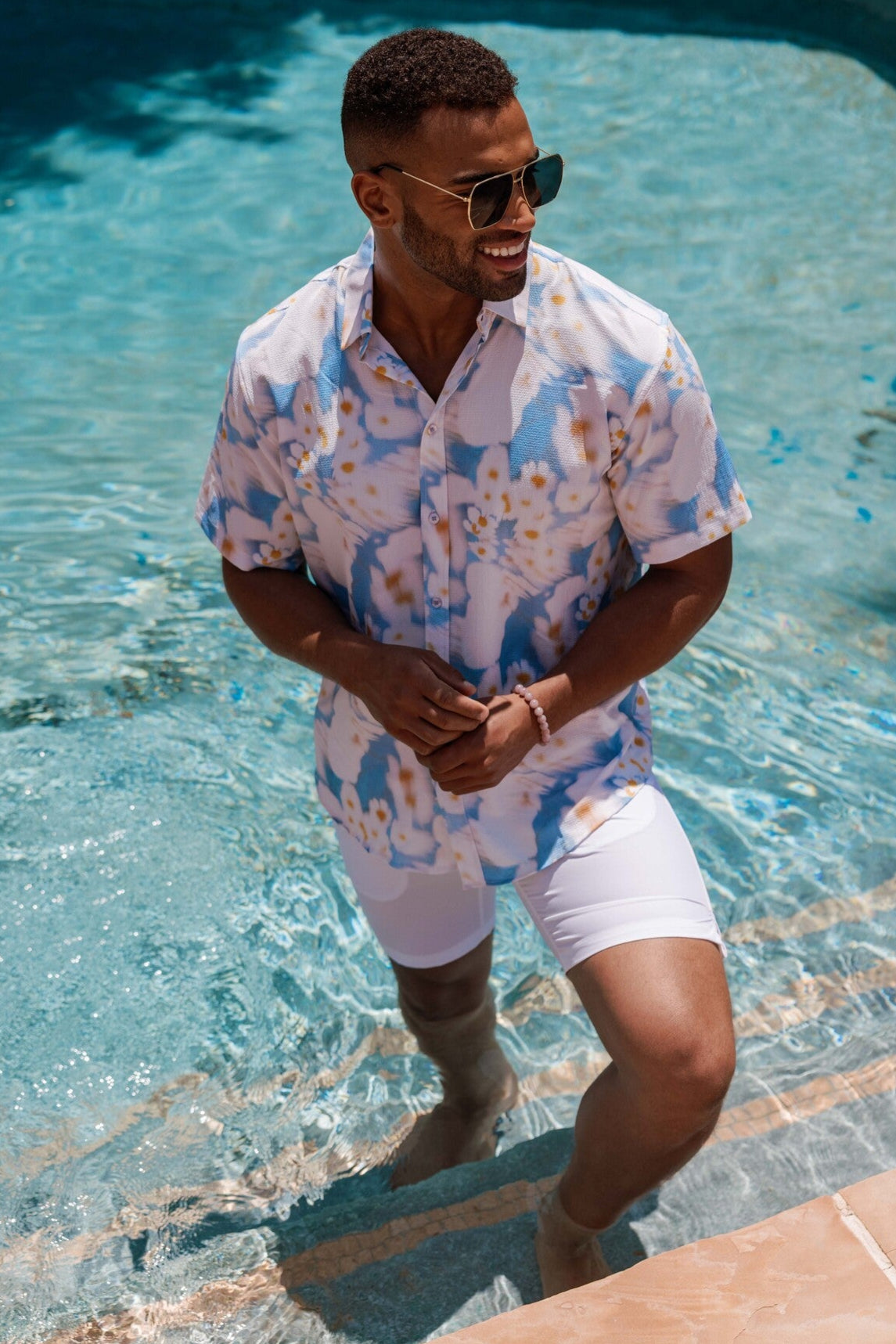 Man in a tie-dye shirt and white shorts standing by a pool