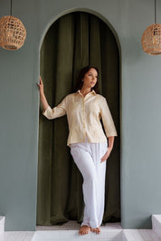 Full body lifestyle shot of a women’s pale yellow linen guayabera paired with white pants for a beach dinner look.