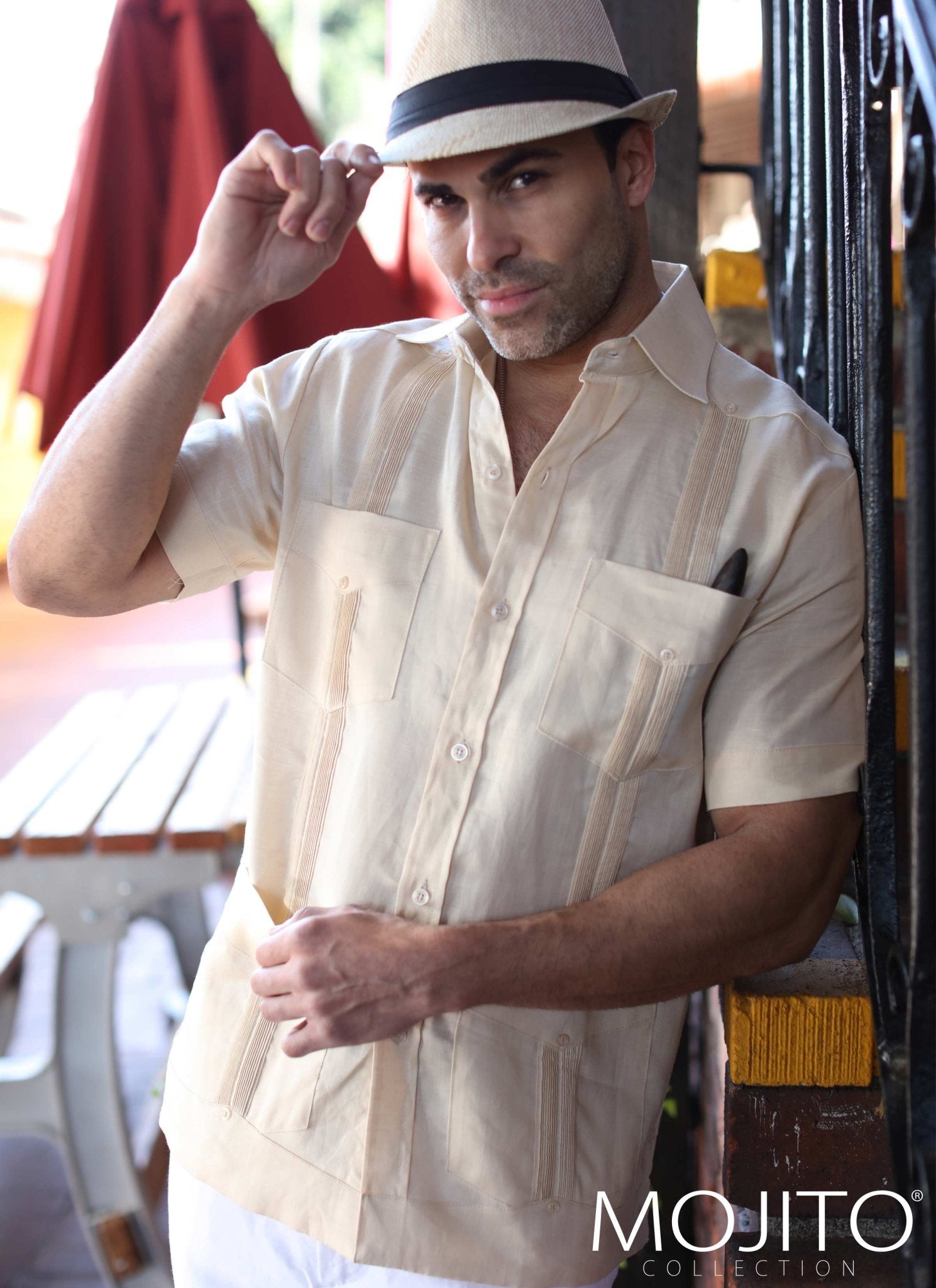 Man in a tan hat and tan linen Guayabera shirt with decorative vertical stripes and chest pockets.