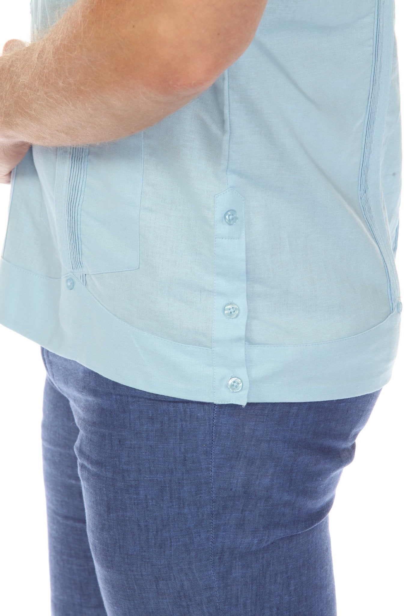 Close-up detail of the lower side hem on the light blue linen guayabera shirt, showing the unique button accent and linen fabric texture.