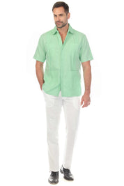Full length shot of a man in a mint green linen guayabera shirt and white linen pants, one hand in his pocket.