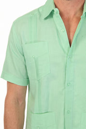 Close-up of the breathable mint green linen fabric, pleats and button detail on the guayabera shirt.