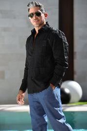 Man wearing a black guayabera and sunglasses standing by a poolside.