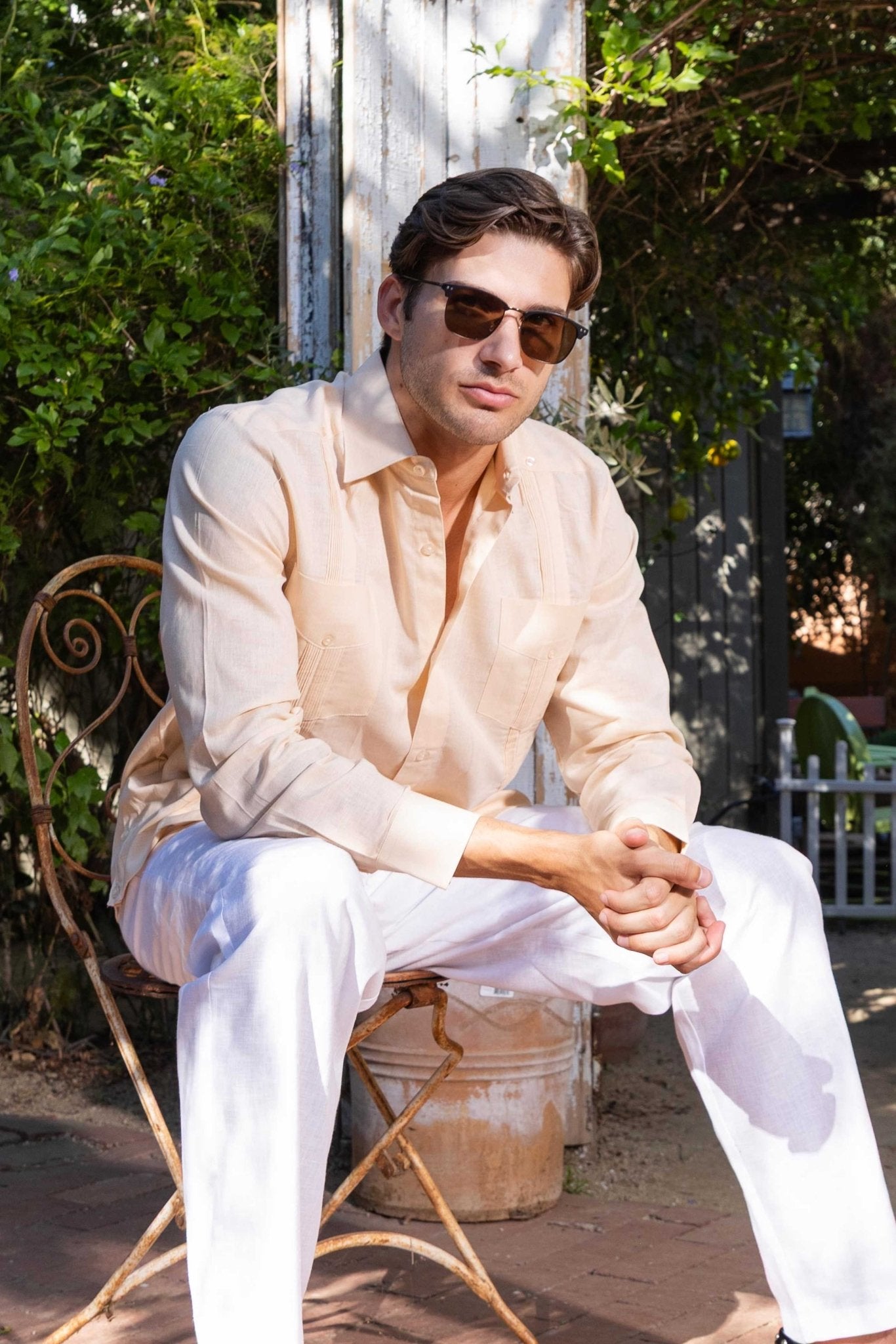 Man wearing a light-colored shirt and white pants sitting outdoors.