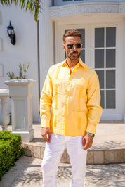 Man wearing a yellow guayabera shirt and white pants standing in front of a building.