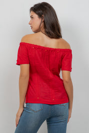Woman wearing a red off-shoulder top and blue jeans against a plain background