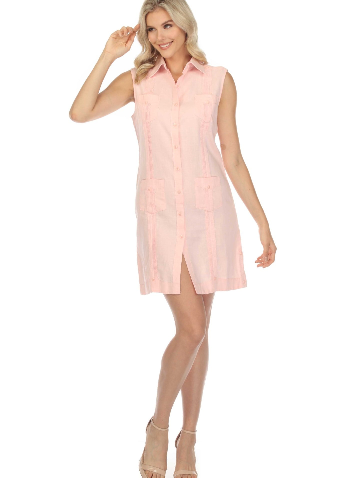 A woman models a pink, sleeveless, button-down, linen guayabera dress shirt with collared neck and front pockets.