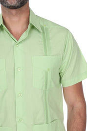 A close-up of a man wearing a light green short-sleeve guayabera button-up shirt with a chest pocket and decorative vertical stitching.