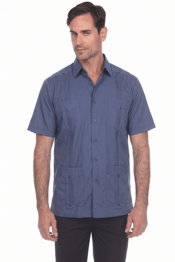 A man wearing a white short-sleeve guayabera-style button-up shirt with four front patch pockets, paired with black pants, photographed against a plain white studio background.