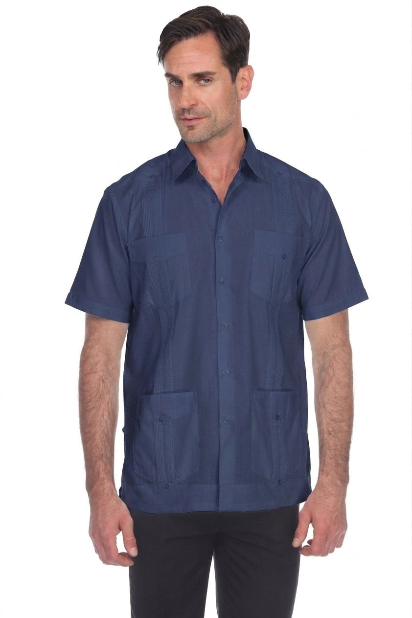 A man wearing a short-sleeve button-up camp shirt in navy blue, paired with black pants, photographed against a solid white background.