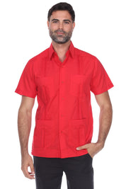 A man wearing a bright red short-sleeve button-up shirt with two chest pockets and four front patch pockets, paired with black pants, against a plain white background.