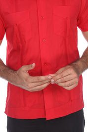 A close-up of a man wearing a bright red short-sleeve button-up shirt with two chest pockets and dark pants, against a plain white background.