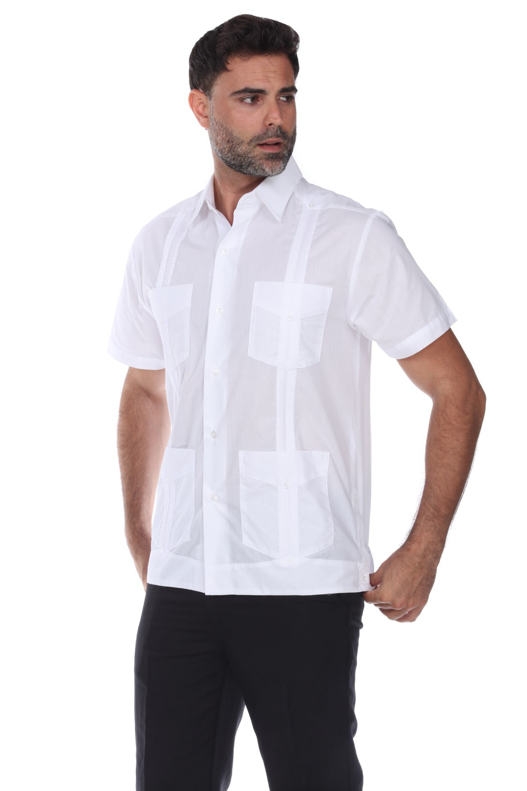 A man wearing a white short-sleeve guayabera-style button-up shirt with four front patch pockets, paired with black pants, photographed against a plain white studio background.