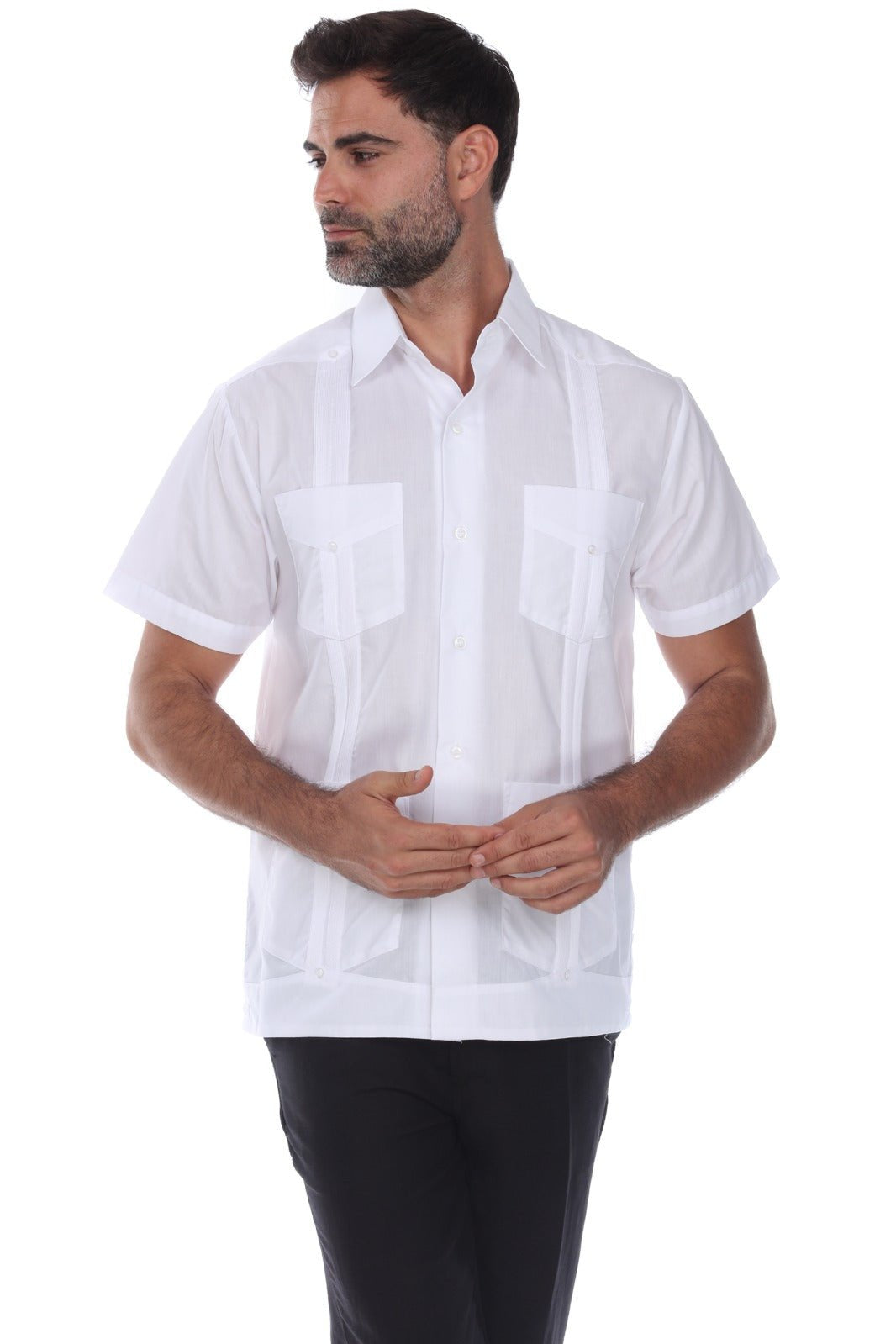 A man wearing a white short-sleeve guayabera-style shirt with decorative vertical pleats and two chest pockets, paired with black pants, against a plain white background.