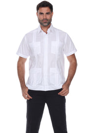 A man wearing a white short-sleeve guayabera-style shirt with vertical pleats and four front patch pockets, paired with black pants, against a plain white background.
