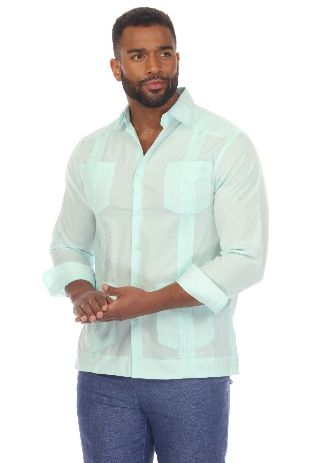 A man wearing a light mint green Guayabera-style button-up shirt with vertical stripes and blue trousers, standing against a plain white background.