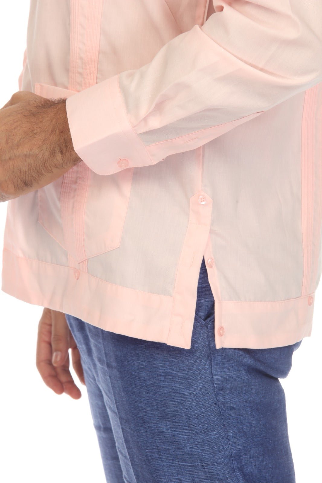 A close-up of a man wearing a light pink guayabera-style shirt with contrasting pink piping and blue pants, shown from the chest down against a white background.